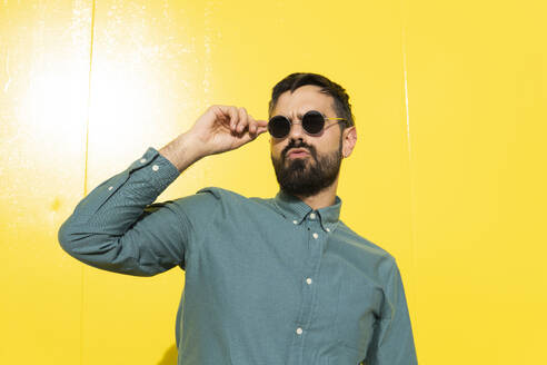 Portrait of a man wearing an aquamarine shirt and sunglasses posing smiling. Yellow background. Granada, Spain. - MGRF01287