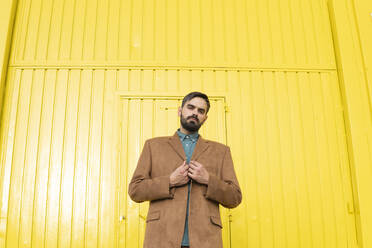 Mann mit brauner Jacke und vor einem gelben Gebäude stehend - MGRF01294