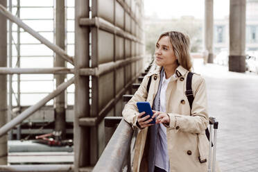 Frau hält Smartphone und steht am Geländer eines Bahnhofs - EBBF08838