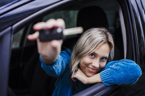 Lächelnde Frau zeigt den Schlüssel eines neuen Autos - EBBF08889
