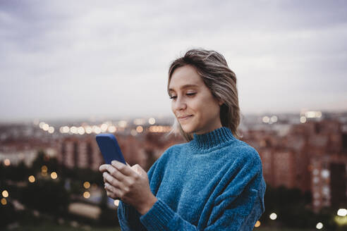 woman using mobile phone over city background at sunset, Madrid, Spain - EBBF08908