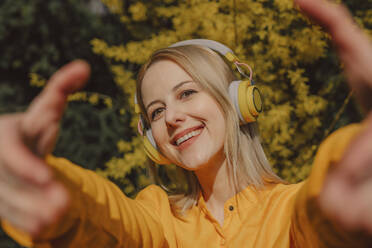 Lächelnde Frau mit gelben drahtlosen Kopfhörern und Gesten an einem sonnigen Tag - VSNF01823