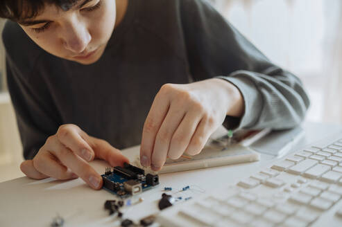 Jugendlicher stellt zu Hause ein elektrisches Bauteil in der Nähe der Tastatur ein - ANAF02818