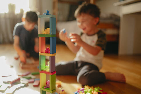 Turm aus Bauklötzen mit spielenden Kindern im Hintergrund zu Hause - ANAF02833