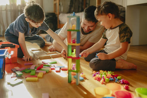 Glückliche Jungen spielen mit Spielzeug in der Nähe des Vaters zu Hause - ANAF02834