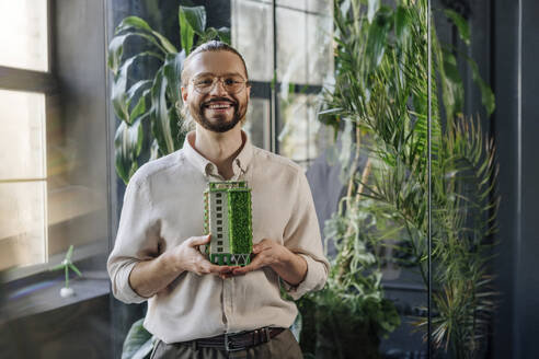 Businessman holding a biophilic architectural model in green office, businessman, office, plants, design, landscape designer, architect, building, workplace, green business, sustainability - YTF02155