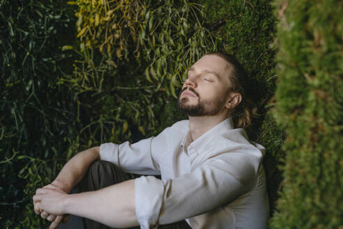Businessman relaxing with eyes closed near plants - YTF02164