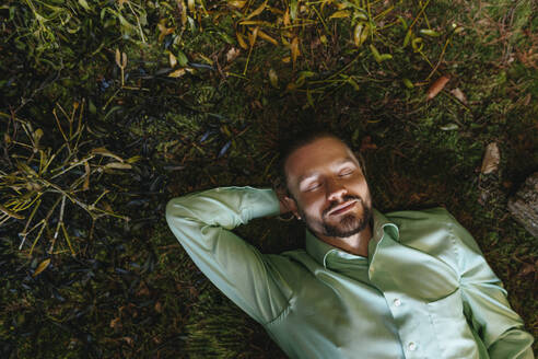 Businessman with eyes closed relaxing on moss - YTF02170