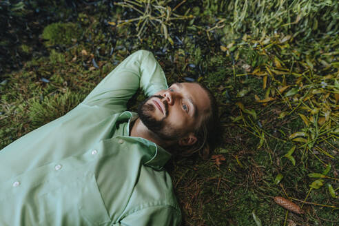 Thoughtful businessman relaxing on moss - YTF02171