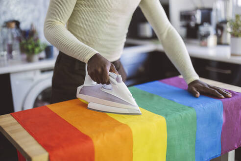 Nicht-binäre Person bügelt Regenbogenflagge zu Hause - JCCMF11622