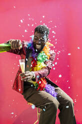 Glückliche nicht-binäre Person gießt Champagner in Glas gegen rosa Hintergrund - JCCMF11674