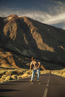 Sporty boy going down a road with a Skate board with the Teide in the background. Tenerife, Canary Islands, Spain. - ACPF01573