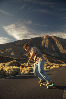 Sporty boy going down a road with a Skate board with the Teide in the background. Tenerife, Canary Islands, Spain. - ACPF01574