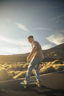 Sporty boy going down a road with a Skate board with the Teide in the background. Tenerife, Canary Islands, Spain. - ACPF01575