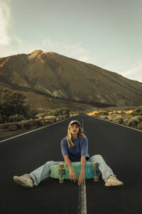 Unbekümmerte Frau mit Skateboard auf einer Bergstraße vor dem Teide - ACPF01580