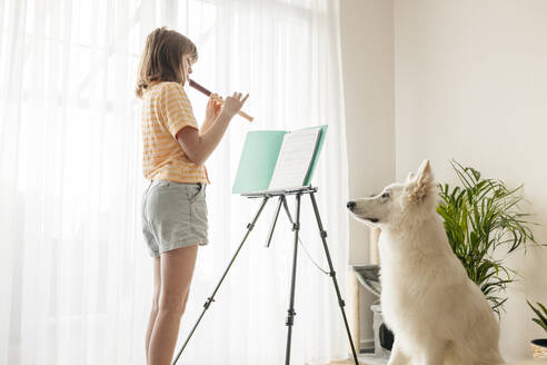 Mädchen spielt Flöte in der Nähe von weißen Schweizer Schäferhund zu Hause - ELMF00192