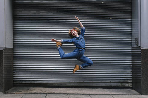 Happy young woman jumping in front of shutter - ASGF04986