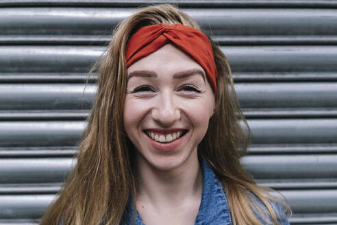 Smiling woman wearing red headband in front of shutter - ASGF04990
