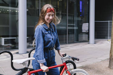 Glückliche junge Frau mit Fahrrad auf der Straße - ASGF04994
