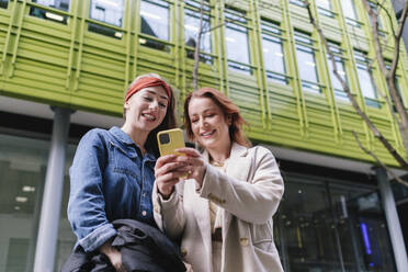 Glückliche Freunde mit Smartphone vor einem Gebäude - ASGF04995