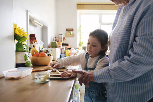 Mädchen schmiert Butter auf Brote mit Mutter zu Hause - ASGF05008