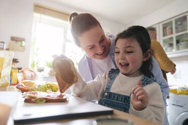 Fröhliche Mutter und Tochter bereiten zu Hause ein Sandwich zu - ASGF05018