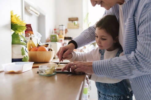 Lächelnde Mutter und Tochter beim Auftragen von Butter in der Küche zu Hause - ASGF05028