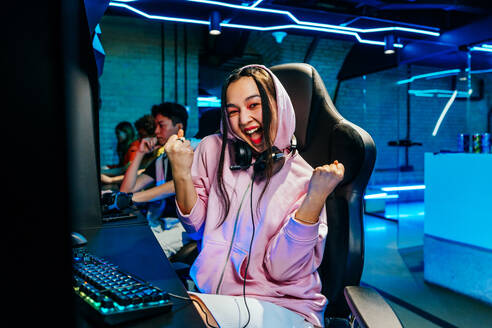 Schöne junge asiatische Frau, die in einem Internetcafé Videospiele spielt - Videospieler, die Spaß am Spielen von E-Sports an einer Computer-Videospielkonsole haben - DMDF11604