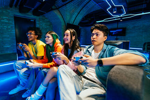 Multiethnische Gruppe junger Freunde, die zu Hause auf dem Sofa sitzend Videospiele spielen - Videospieler haben Spaß beim E-Sport an einer Computer-Videospielkonsole - DMDF11690