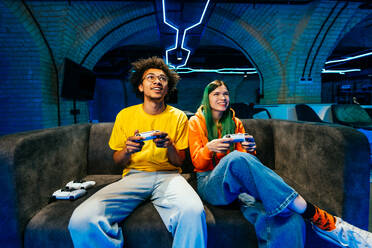 Multiethnische Gruppe junger Freunde, die zu Hause auf dem Sofa sitzend Videospiele spielen - Videospieler haben Spaß beim E-Sport an einer Computer-Videospielkonsole - DMDF11695