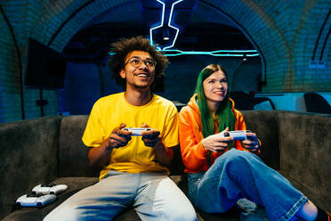 Multiethnische Gruppe junger Freunde, die zu Hause auf dem Sofa sitzend Videospiele spielen - Videospieler haben Spaß beim E-Sport an einer Computer-Videospielkonsole - DMDF11696