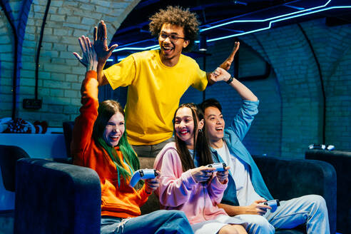 Multiethnische Gruppe junger Freunde, die zu Hause auf dem Sofa sitzend Videospiele spielen - Videospieler haben Spaß beim E-Sport an einer Computer-Videospielkonsole - DMDF11709