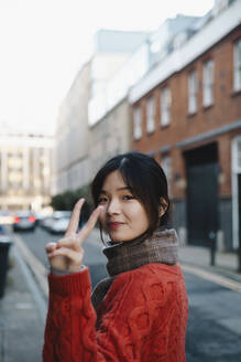 Young woman gesturing peace sign on street - AMWF02153