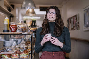 Lächelnde Geschäftsfrau, die in der Nähe der Lebensmittelauslage in einem Café steht - AMWF02177