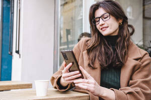 Lächelnde Geschäftsfrau mit Smartphone in einem Straßencafé - AMWF02178