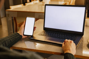 Geschäftsfrau hält Smartphone neben Laptop im Büro - AMWF02183
