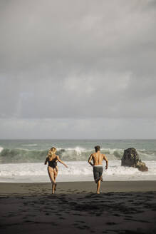 Couple running backwards about to enter the sea during a cloudy day. Tenerife, Canary Islands, Spain - ACPF01584