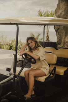 Girl posing sitting in a golf cart with a view of the sea in the background. Tenerife, Canary Islands, Spain. - ACPF01589