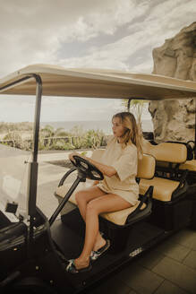 Girl posing sitting in a golf cart with a view of the sea in the background. Tenerife, Canary Islands, Spain. - ACPF01591