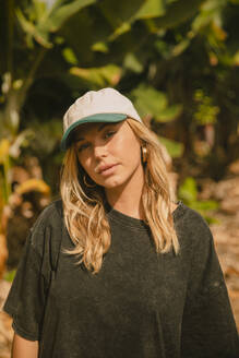 Blonde girl with a cap in front of some banana trees looking at the camera. Tenerife, Canary Islands, Spain - ACPF01601