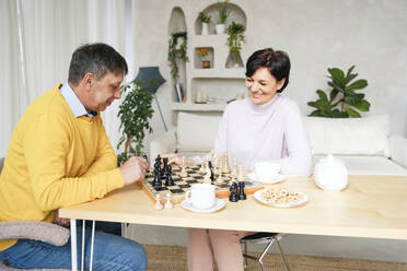 Couple playing chess at table in living room - NLAF00404