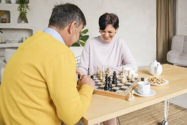 Mature couple playing chess on table at home - NLAF00405