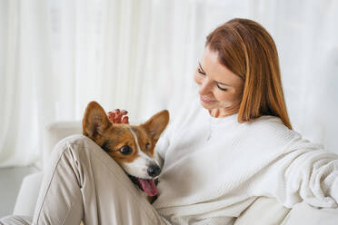 Smiling woman sitting with dog in living room - NLAF00438