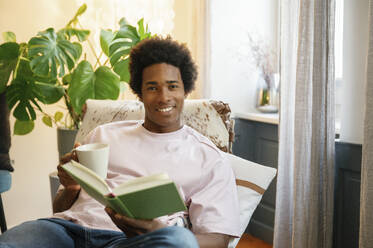young handsome man holding a book, looking at camera and smiling - FLMZF00048