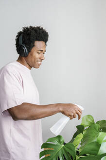 young man listening music and watering plant - FLMZF00058