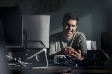 Smiling mature businessman sitting near desktop PC at desk in office - JOSEF24126