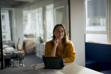 Thoughtful businesswoman sitting with tablet PC at desk in office - JOSEF24133