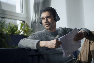 Businessman wearing headset and holding documents in office - JOSEF24175