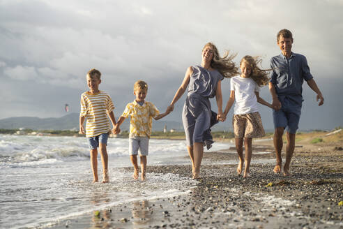 Family holding hands together walking on shore at beach - NJAF00948