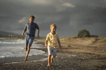 Father and son running on shore at beach - NJAF00964